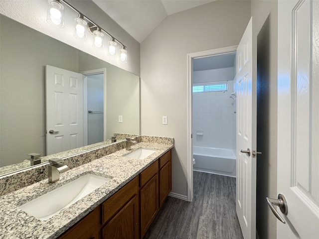 full bathroom with tiled shower / bath combo, vanity, wood-type flooring, vaulted ceiling, and toilet