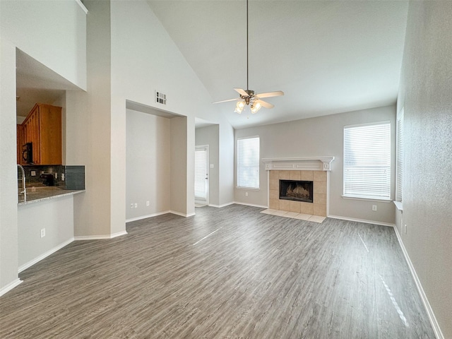 unfurnished living room featuring hardwood / wood-style floors, ceiling fan, high vaulted ceiling, and a tiled fireplace