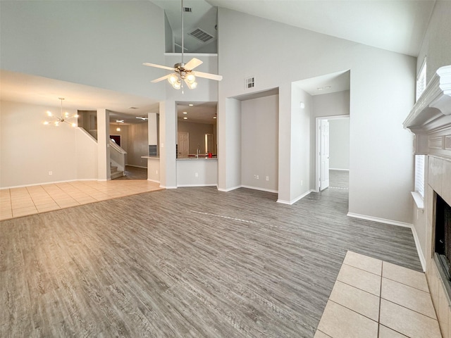 unfurnished living room with tile patterned flooring, sink, ceiling fan with notable chandelier, and high vaulted ceiling