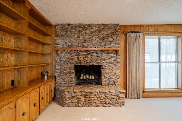 living room with a textured ceiling, wooden walls, a stone fireplace, and light colored carpet