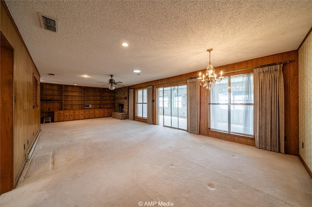 unfurnished living room with a textured ceiling, wooden walls, light carpet, ceiling fan with notable chandelier, and visible vents