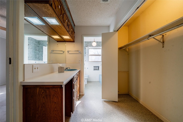 kitchen with a textured ceiling, a sink, baseboards, light countertops, and brown cabinets