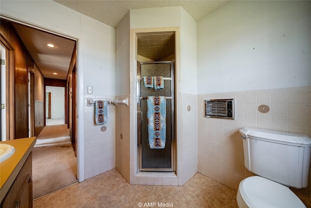 bathroom with a stall shower, wainscoting, toilet, a textured ceiling, and tile walls