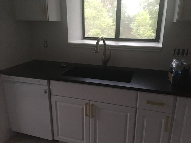 kitchen featuring dark countertops, white dishwasher, a sink, and white cabinetry