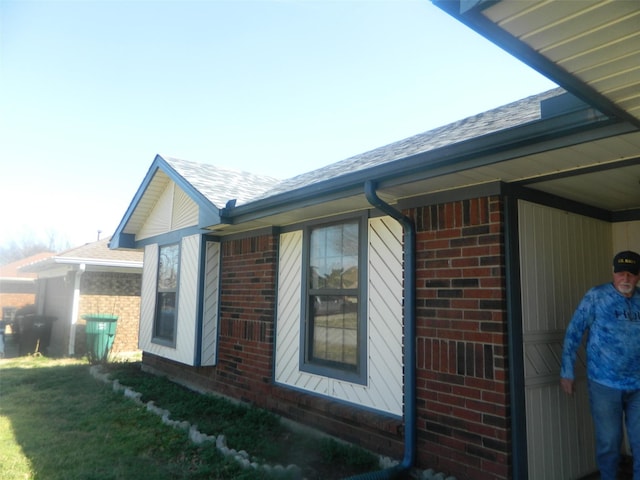 view of property exterior featuring a shingled roof, brick siding, and a lawn