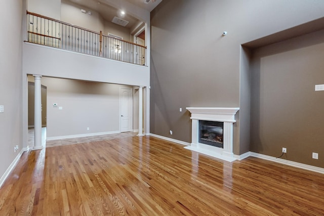 unfurnished living room featuring ornate columns, a towering ceiling, and hardwood / wood-style floors