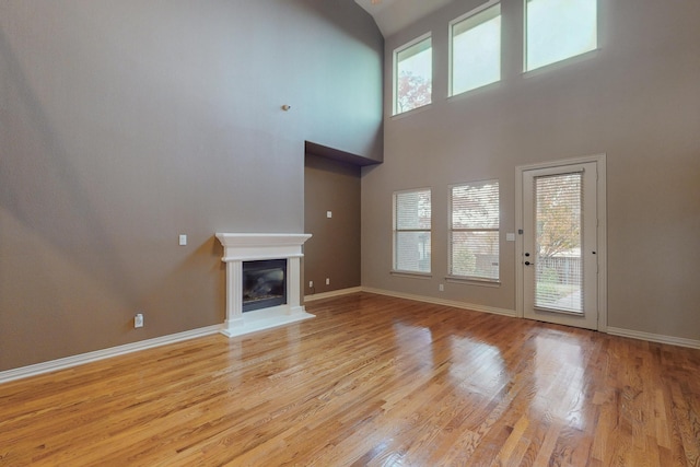 unfurnished living room with light hardwood / wood-style flooring, a healthy amount of sunlight, and a high ceiling