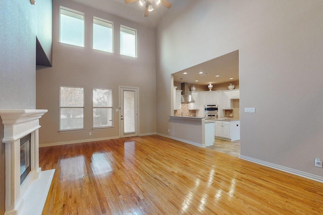 unfurnished living room featuring a high ceiling, ceiling fan, a fireplace, and light hardwood / wood-style floors