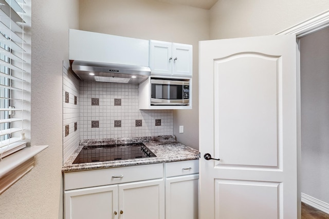 kitchen featuring stainless steel microwave, tasteful backsplash, white cabinets, exhaust hood, and black electric cooktop