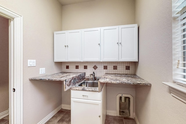 kitchen featuring sink, tasteful backsplash, light stone counters, white cabinets, and dark tile patterned flooring