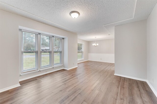 unfurnished room featuring wood-type flooring, a textured ceiling, and an inviting chandelier