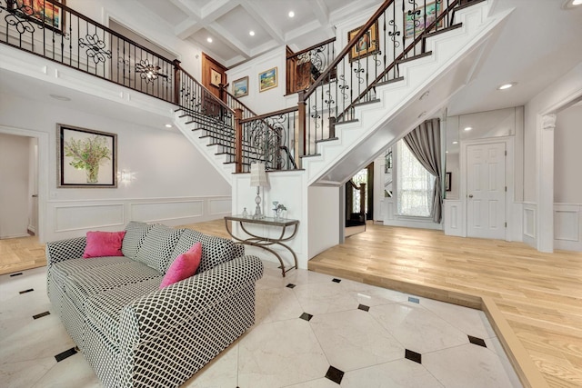 entryway with beam ceiling, a towering ceiling, coffered ceiling, ornamental molding, and light wood-type flooring