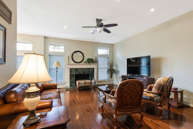 living room with dark wood-type flooring, ceiling fan, a tile fireplace, and a textured ceiling