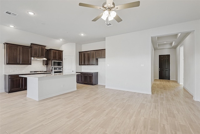 kitchen featuring appliances with stainless steel finishes, backsplash, dark brown cabinetry, light hardwood / wood-style floors, and an island with sink