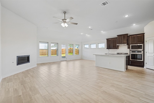 kitchen featuring light hardwood / wood-style flooring, ceiling fan, a kitchen island with sink, stainless steel appliances, and decorative backsplash