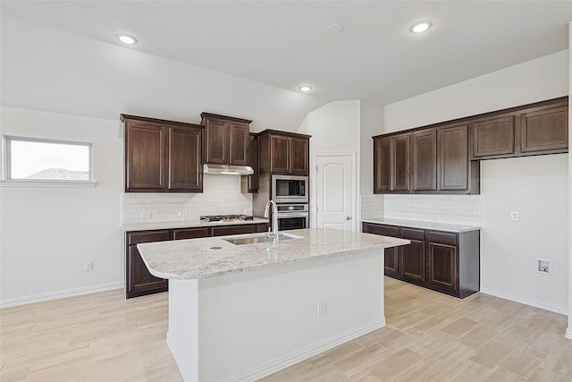 kitchen featuring sink, stainless steel appliances, light stone counters, a center island with sink, and vaulted ceiling