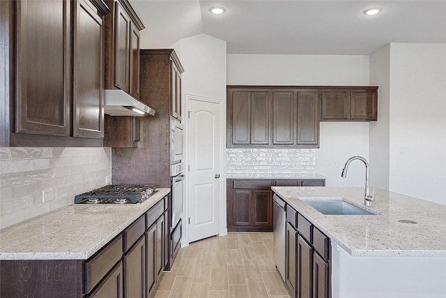 kitchen featuring sink, appliances with stainless steel finishes, an island with sink, light stone countertops, and backsplash