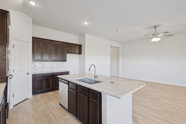 kitchen featuring sink, dishwasher, backsplash, light stone countertops, and an island with sink