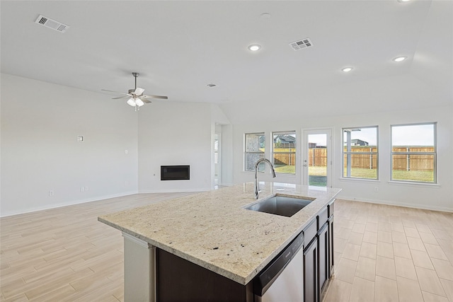 kitchen with sink, stainless steel dishwasher, a kitchen island with sink, and light stone counters