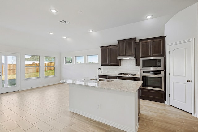 kitchen featuring light stone counters, sink, stainless steel appliances, and an island with sink