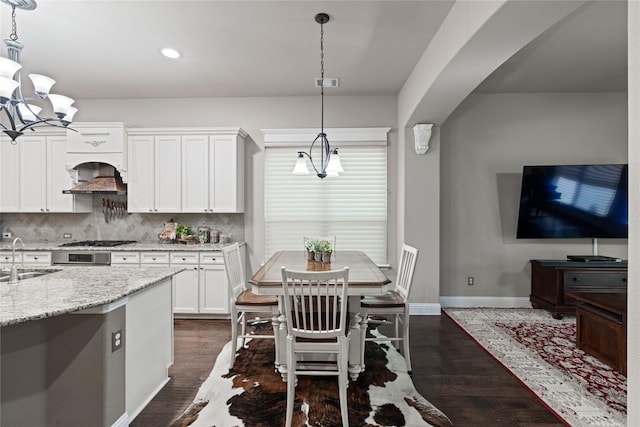 kitchen with white cabinets, hanging light fixtures, light stone counters, tasteful backsplash, and dark hardwood / wood-style flooring