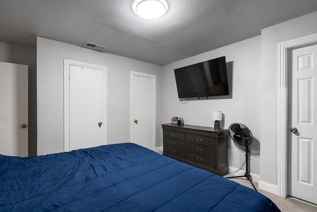 bedroom featuring a textured ceiling, light carpet, and two closets