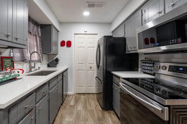 kitchen with appliances with stainless steel finishes, sink, light wood-type flooring, decorative backsplash, and a textured ceiling