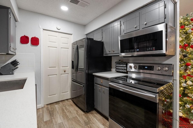 kitchen with sink, gray cabinets, a textured ceiling, appliances with stainless steel finishes, and light hardwood / wood-style floors