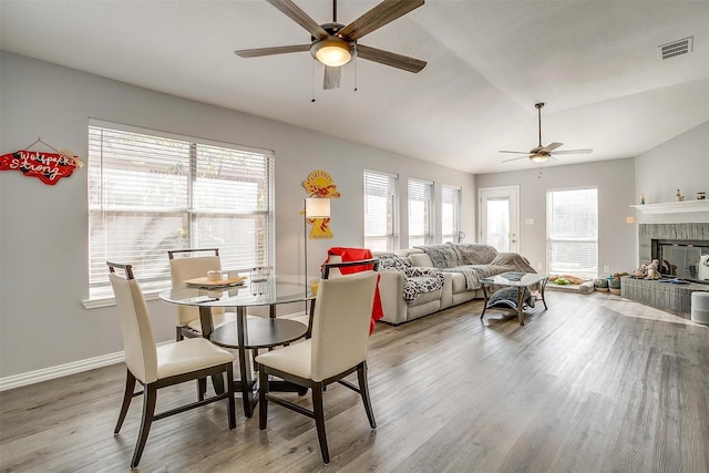 dining room with ceiling fan, hardwood / wood-style floors, lofted ceiling, and a brick fireplace