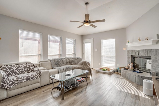 living room featuring ceiling fan, light hardwood / wood-style floors, and a brick fireplace