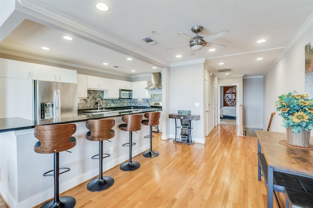 kitchen with white cabinetry, wall chimney range hood, crown molding, light hardwood / wood-style floors, and appliances with stainless steel finishes