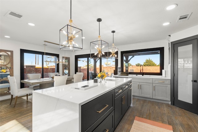 kitchen featuring sink, crown molding, a center island with sink, dark hardwood / wood-style flooring, and pendant lighting