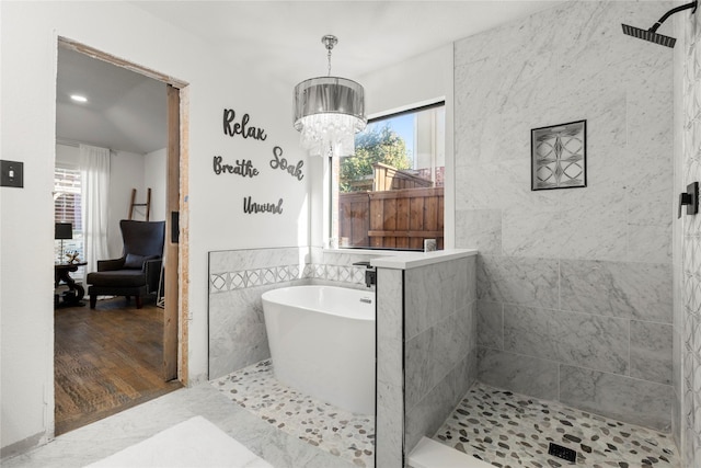 bathroom with tile walls, shower with separate bathtub, and a chandelier