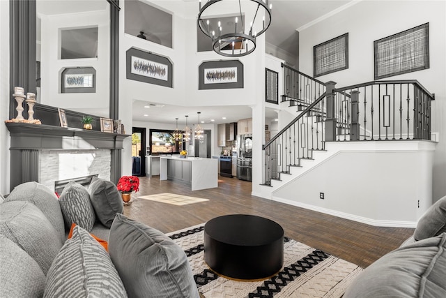 living room featuring dark hardwood / wood-style floors, a towering ceiling, a fireplace, crown molding, and an inviting chandelier