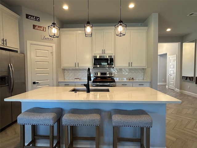 kitchen featuring appliances with stainless steel finishes, sink, decorative light fixtures, white cabinetry, and an island with sink