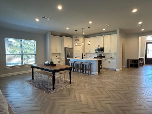 kitchen with a kitchen island with sink, white cabinets, pendant lighting, and appliances with stainless steel finishes