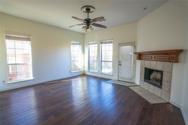 unfurnished living room featuring ceiling fan, dark hardwood / wood-style flooring, a wealth of natural light, and a tiled fireplace