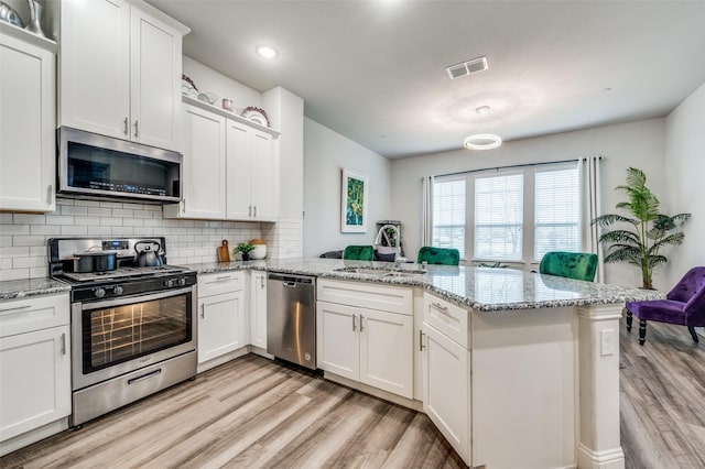 kitchen with kitchen peninsula, appliances with stainless steel finishes, white cabinets, and sink