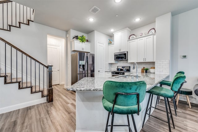 kitchen with sink, a kitchen breakfast bar, kitchen peninsula, white cabinets, and appliances with stainless steel finishes