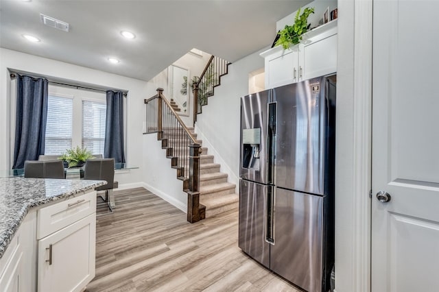 kitchen featuring white cabinetry, stainless steel fridge, light hardwood / wood-style flooring, and light stone counters