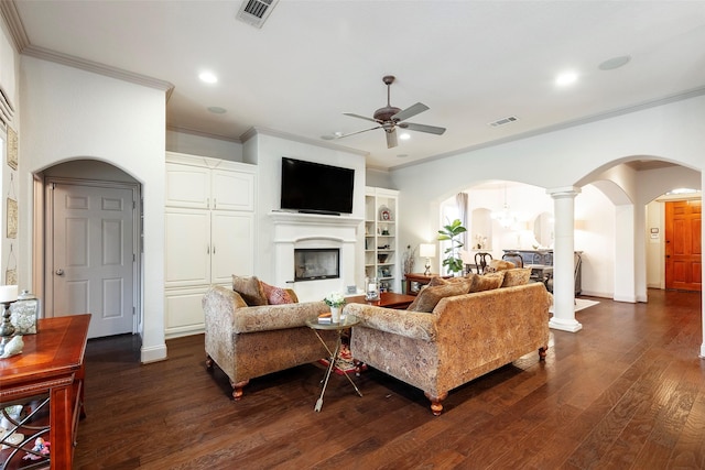 living room with dark wood-type flooring, crown molding, ceiling fan, ornate columns, and built in features