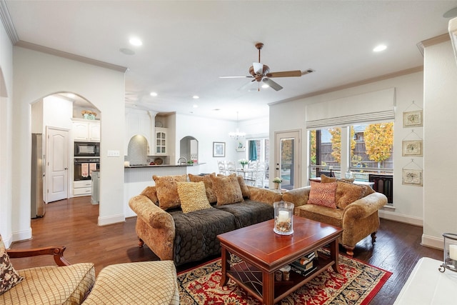 living room with ceiling fan with notable chandelier, ornamental molding, and dark wood-type flooring