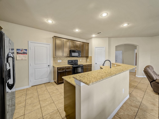 kitchen with dark brown cabinetry, light tile patterned flooring, black appliances, and a center island with sink