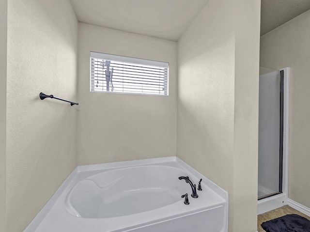 bathroom featuring a textured wall, a stall shower, and a garden tub