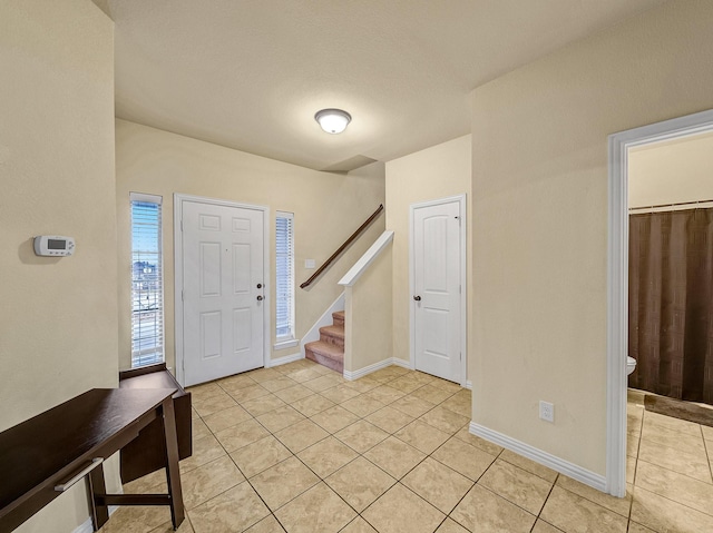 foyer entrance with light tile patterned floors, stairs, and baseboards