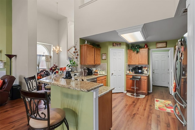 kitchen featuring stainless steel refrigerator, light stone counters, kitchen peninsula, a breakfast bar area, and light wood-type flooring