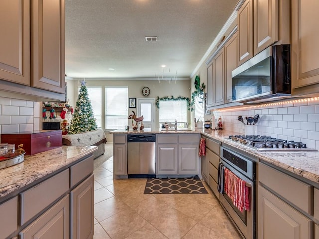 kitchen with appliances with stainless steel finishes, tasteful backsplash, light stone counters, and crown molding