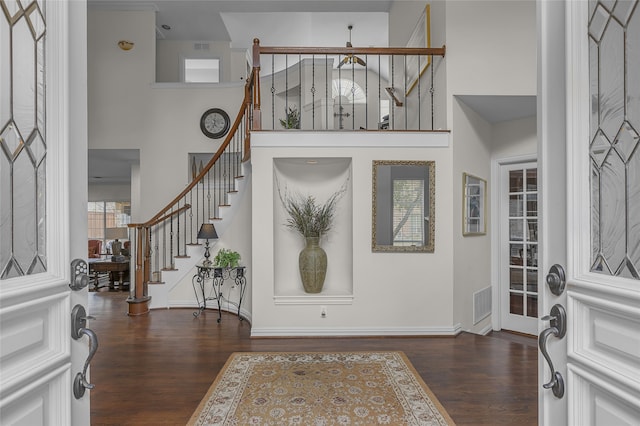 foyer with dark wood finished floors, a towering ceiling, and stairs