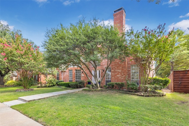 view of property hidden behind natural elements with a front yard, brick siding, and a chimney