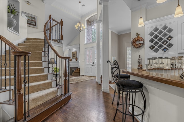 foyer entrance with a bar, ornate columns, dark wood-type flooring, and crown molding